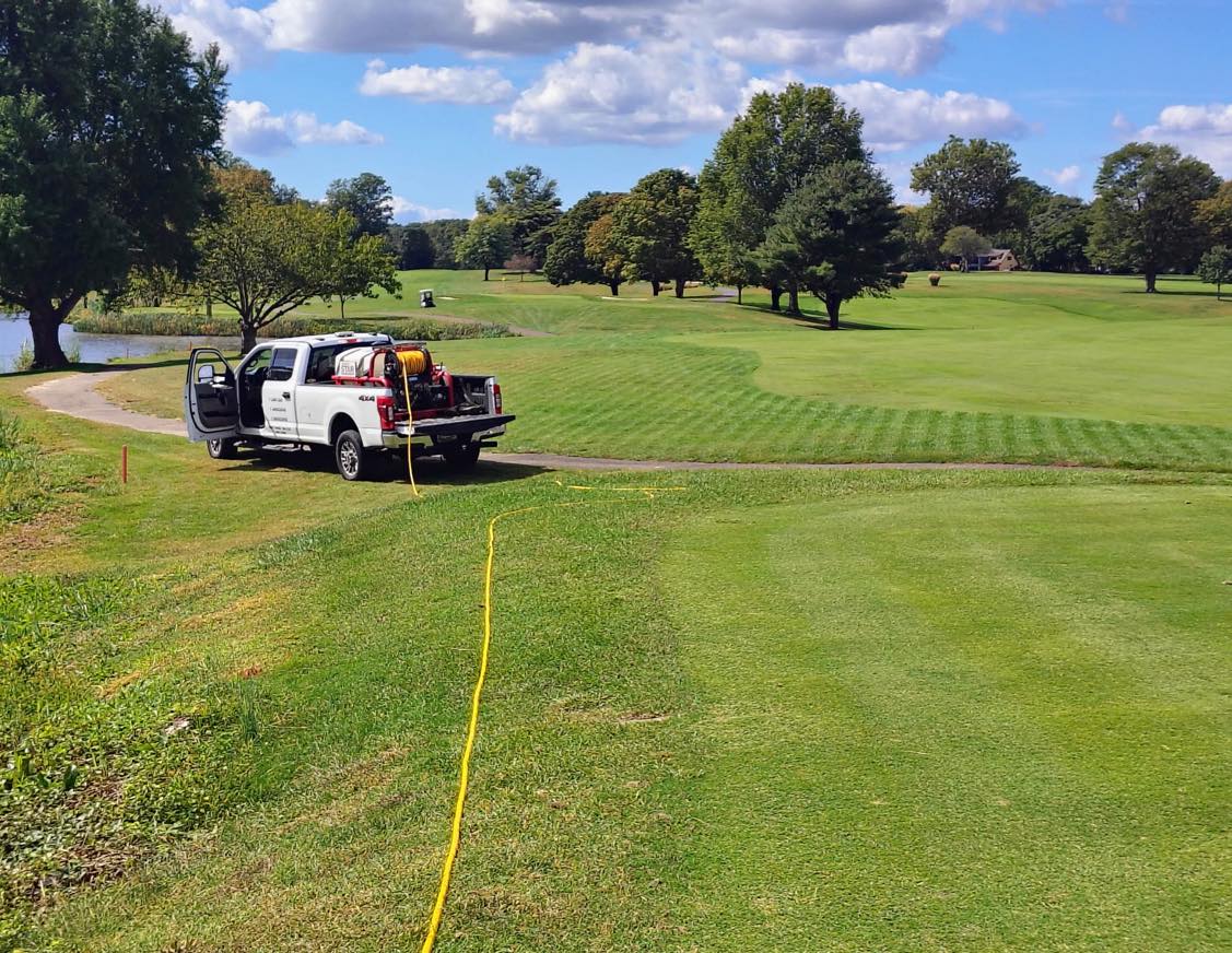 Marshall Property Management spray truck on a golf course fairway with a stormwater pond and its planted edge on the left