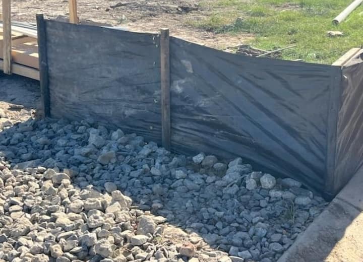 Silt fence staked behind a stone apron on a construction site